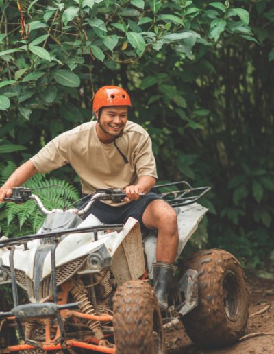 handsome asian man smiling while riding the atv through the difficult terrain