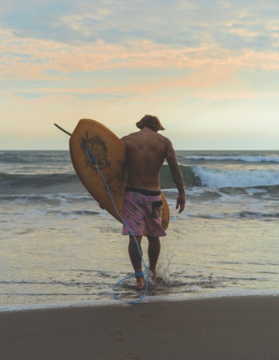 A surfer man walks with a board on a sandy beach. Handsome young